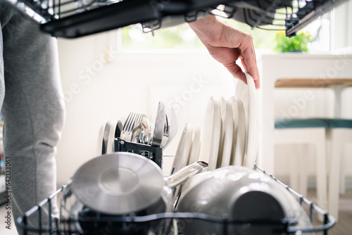 Dish washing machine. Washer in kitchen. Man using dishwasher and unloading clean plates and cutlery. Family housework. Household chores. Utensils in basket and kitchenware in rack. Full load.