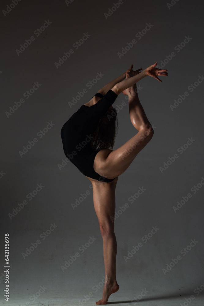 Naklejka premium Flexible sexy girl dancing. Beautiful flexible woman body. Fashion art studio portrait of fit sexy flexible woman on black. Gymnastic slim and flexible dancer woman performing. Stretches exercise.