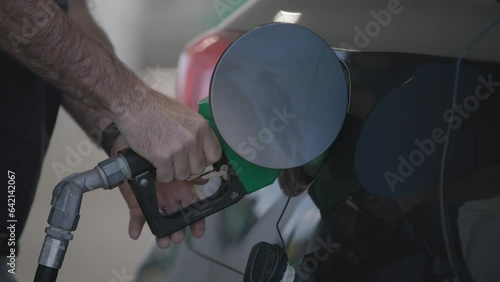 Slow motion of man and his hands filling his automobile car tank with unleaded gas and petroleum fuel at small gas station in close up on grey vehicle
