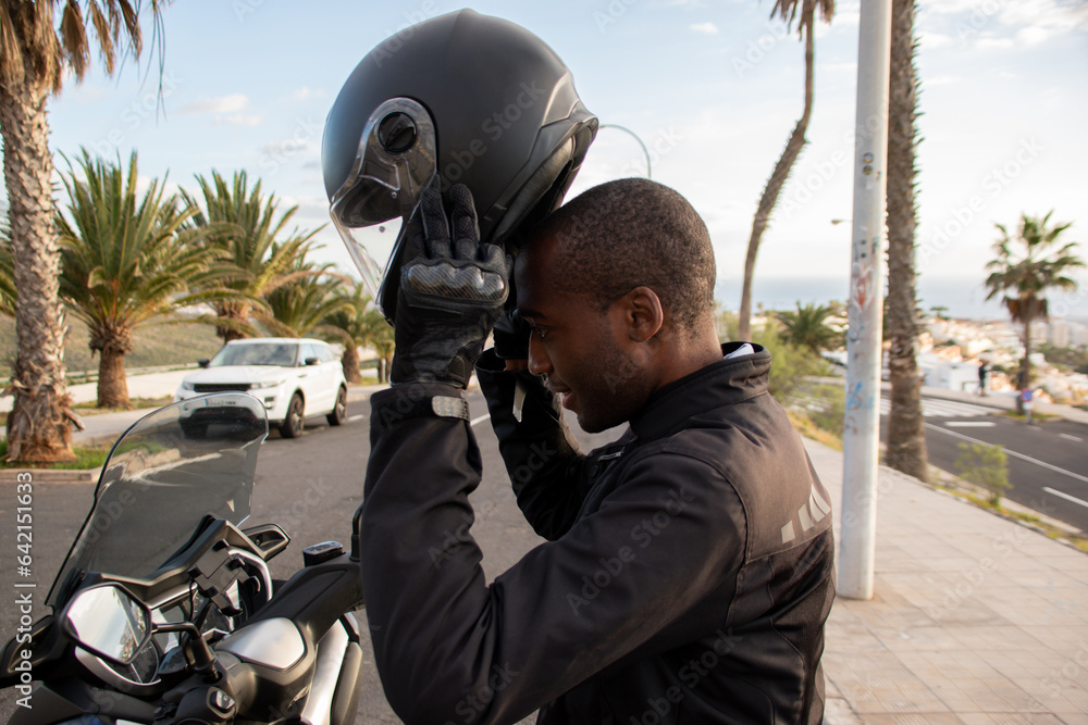 Obraz na plátně Smiling african american biker putting on full face helmet