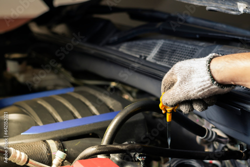 Mechanic checks car lubricant or from gray bottle on background of engine Oil change service, auto repair shop Technology and transportation industry