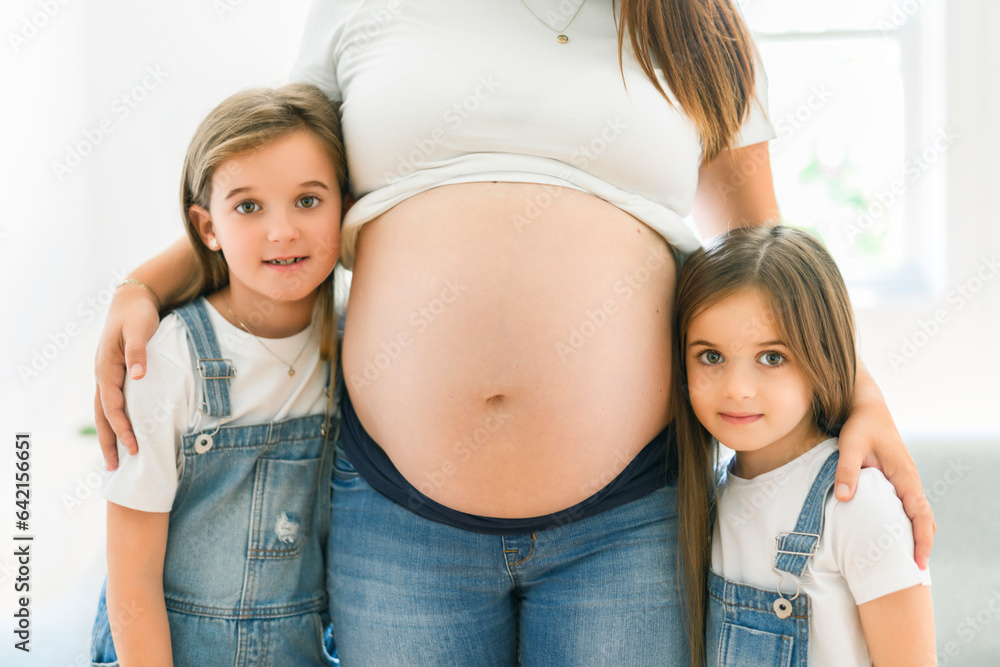 Excited two little daughter with pregnant mom tummy at home Excited two little daughter with pregnant mom tummy at home