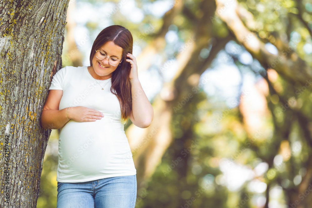 Pregnant woman posing in the park . Portrait of a happy and proud pregnant woman looking at her belly Pregnant woman posing in the park . Portrait of a happy and proud pregnant woman looking at her belly