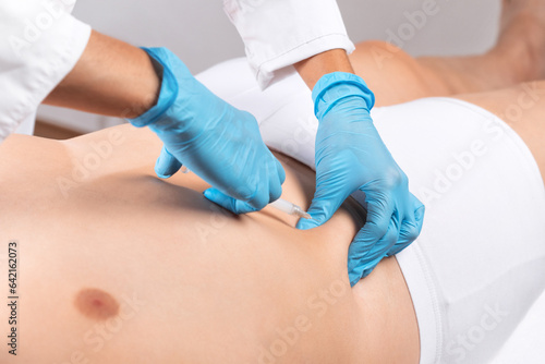 A beautician makes lipolytic injections to burn fat on a man's belly. Male aesthetic cosmetology in a beauty salon.