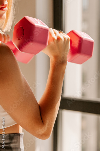 Unrecognizable beautiful young fit caucasian woman exercising with pink dumbbells indoors