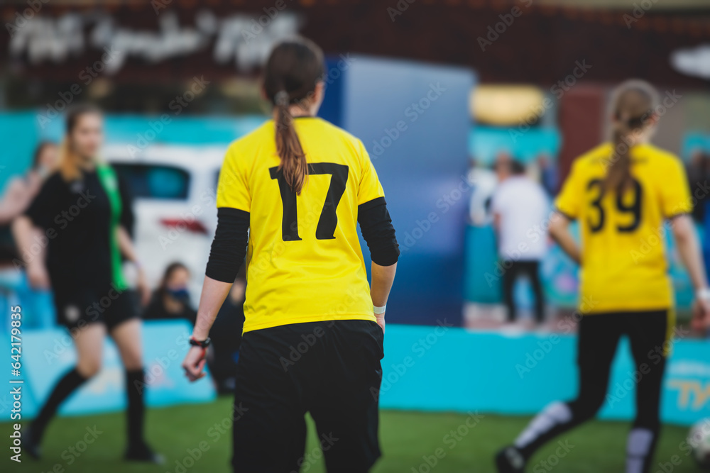 Fototapeta premium Female football street match outdoor game on an artificial astroturf lawn, girls play soccer game on a pitch field, young women participate in football competition on a stadium with green grass