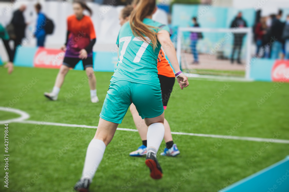 Female football street match outdoor game on an artificial astroturf lawn, girls play soccer game on a pitch field, young women participate in football competition on a stadium with green grass