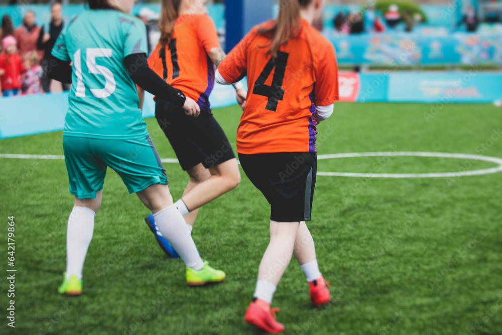 Fototapeta premium Female football street match outdoor game on an artificial astroturf lawn, girls play soccer game on a pitch field, young women participate in football competition on a stadium with green grass