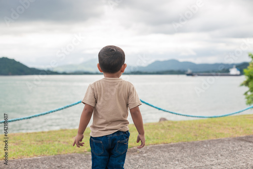 latin boy standing with his back facing the sea, wearing a khaki sweater