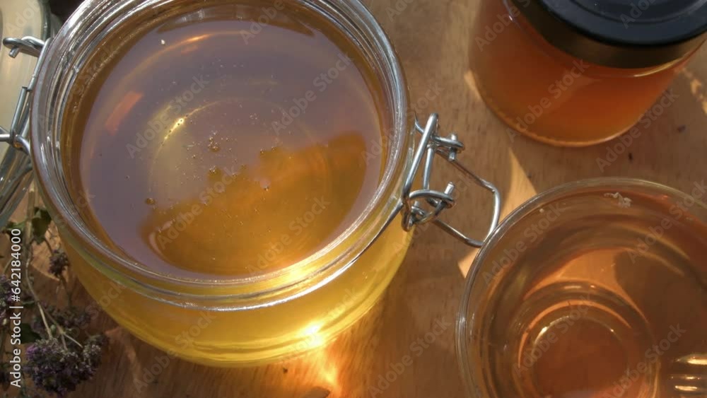 beautiful fresh natural golden linden honey in big glass jar at wooden tray with sunny light inside. close up beautiful fresh natural golden linden honey in big glass jar at wooden tray with sunny light inside. close up
