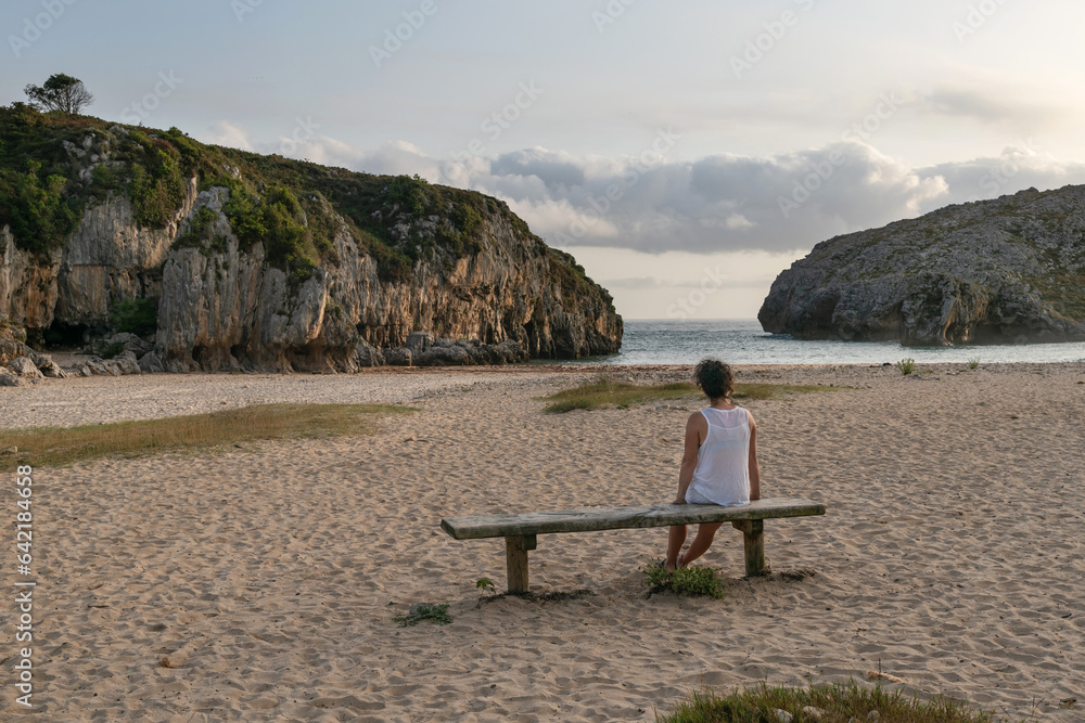 Fototapeta premium Woman sitting on Cuevas del Mar Beach. Council of Llanes, Asturias