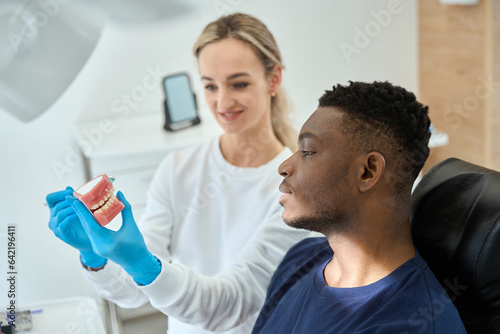 Smiling nurse showing model of teeth to male