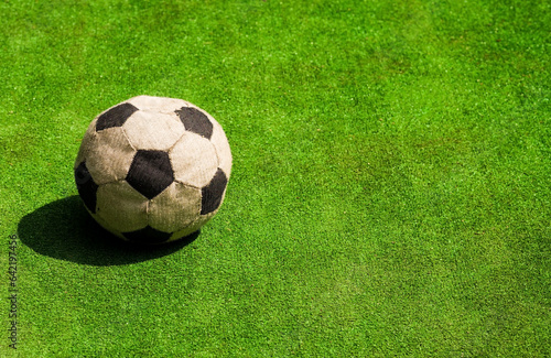 The old shabby soccerball on a green background. Old soccer (football) ball on green field, in the fall on asphalt.