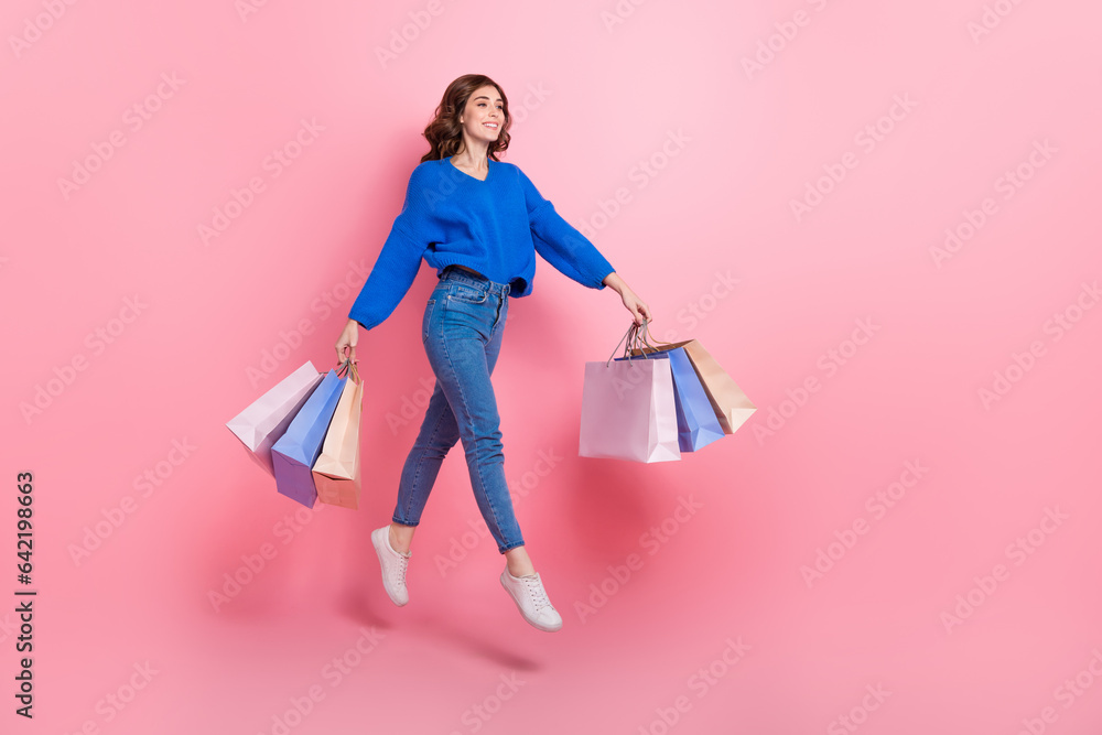 Full size profile photo of gorgeous energetic girl hold mall bags jump run empty space isolated on pink color background
