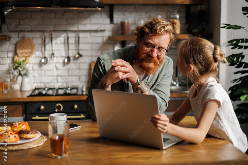 Father and daughter talking near laptop, pastry and drinks in kitchen Father and daughter talking near laptop, pastry and drinks in kitchen