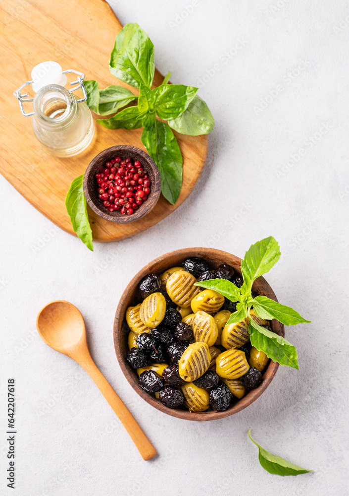 A set of green and black dried olives in wooden  bowl on a light background with olive oil and basil. The concept of vegetarian healthy snacks.