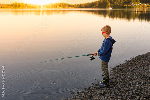 Little boy fishing on a moutain lake at sunset