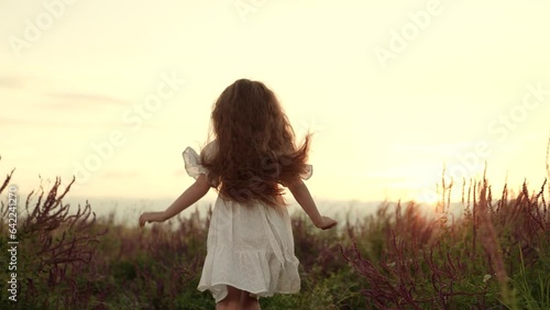 Happy little girl runs enjoying freedom in field at summer sunset backside view photo