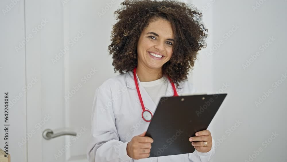 Young beautiful hispanic woman doctor reading document on clipboard smiling at clinic Young beautiful hispanic woman doctor reading document on clipboard smiling at clinic
