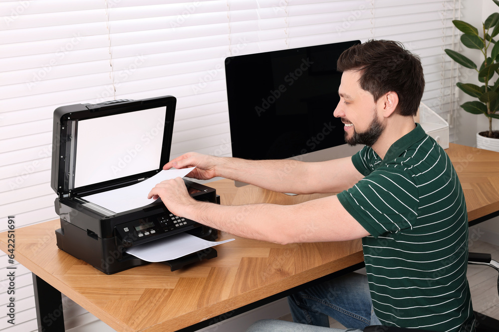 Man using modern printer at wooden table indoors