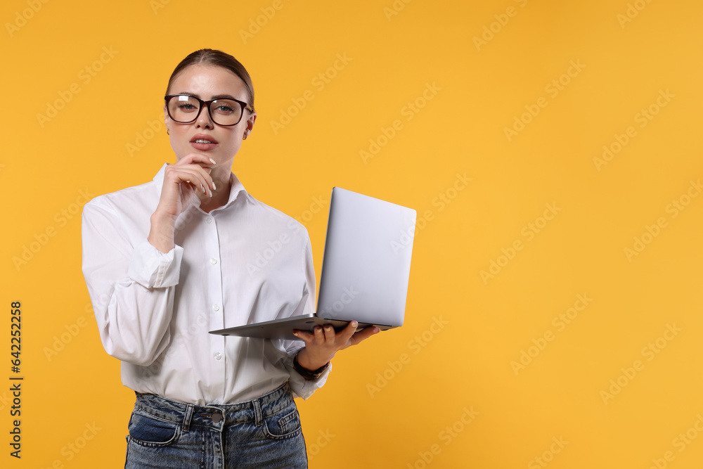 Thoughtful woman in glasses with laptop on orange background. Space for text
