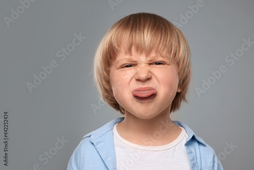 Cute little boy showing his tongue on grey background. Space for text