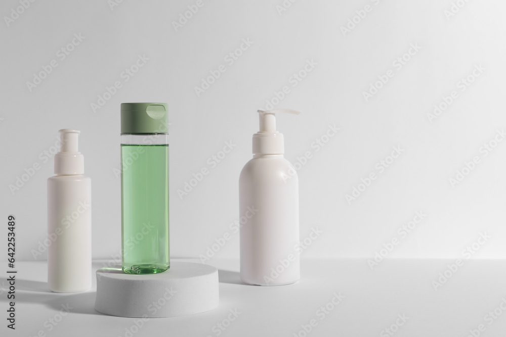 Bottles with different cosmetic products and podium on white background, space for text Bottles with different cosmetic products and podium on white background, space for text