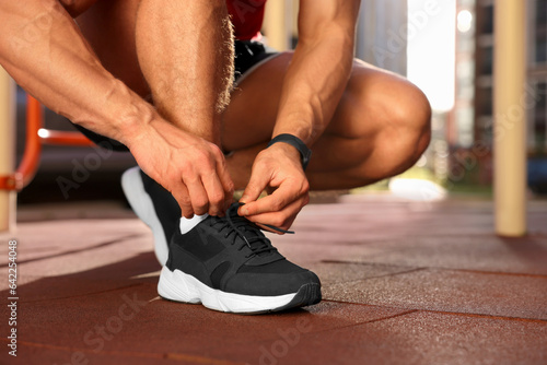 Man tying shoelaces before training at outdoor gym on sunny day, closeup