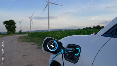 Electric car recharging energy from EV charging station display futuristic smart battery status hologram by EV charger plug cable in wind turbine farm. Alternative clean energy sustainability. Peruse © Summit Art Creations