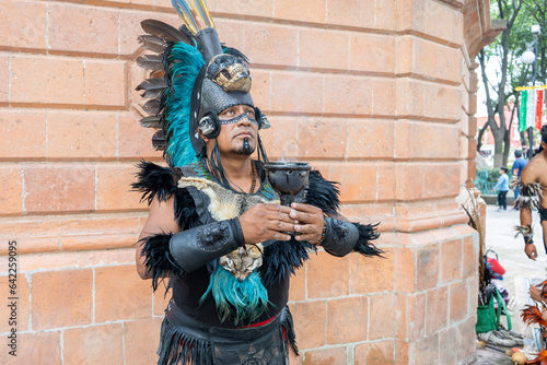 concentrated shaman using a calyx o chalice, aztec dancer with feathered headdress and skulls on his costume, hispanic culture mexican traditional performer