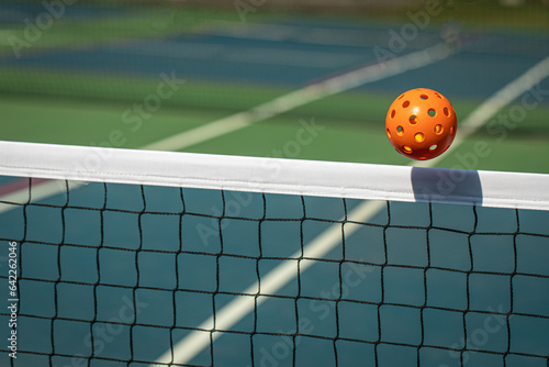 Orange Pickleball crossing a Pickleball net with shadow on the top tape.