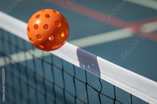 Orange Pickleball crossing a Pickleball net with shadow on the top tape.