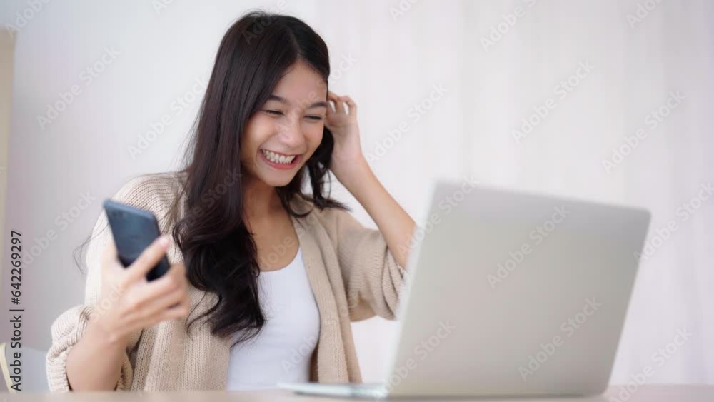 Young asian woman happy working on computer laptop and hand typing chat message on mobile smartphone at home. Video call, Online meeting Young asian woman happy working on computer laptop and hand typing chat message on mobile smartphone at home. Video call, Online meeting