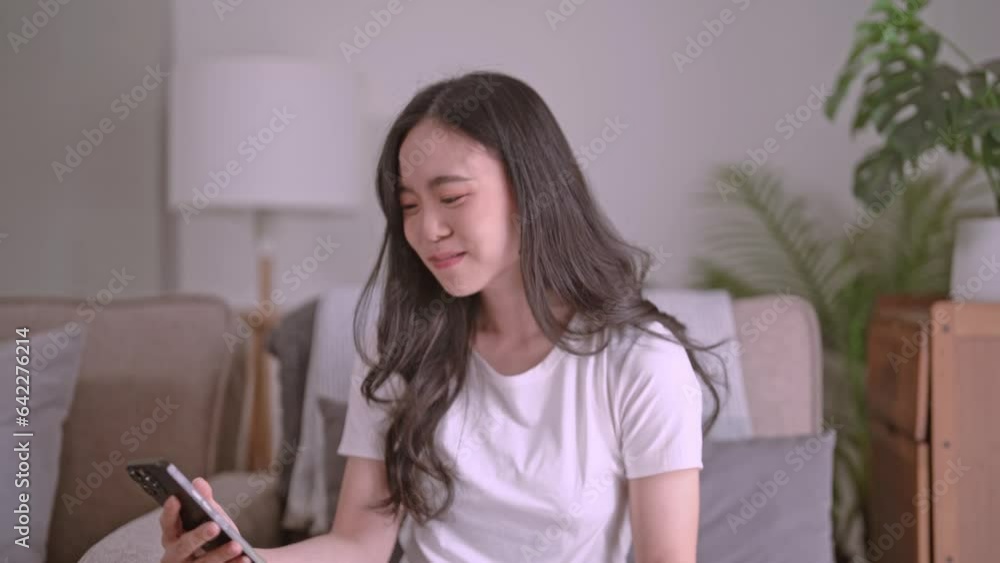 Asian woman eating potato chips while using mobile phone to watching variety show and relax sits at home. Asian woman eating potato chips while using mobile phone to watching variety show and relax sits at home.