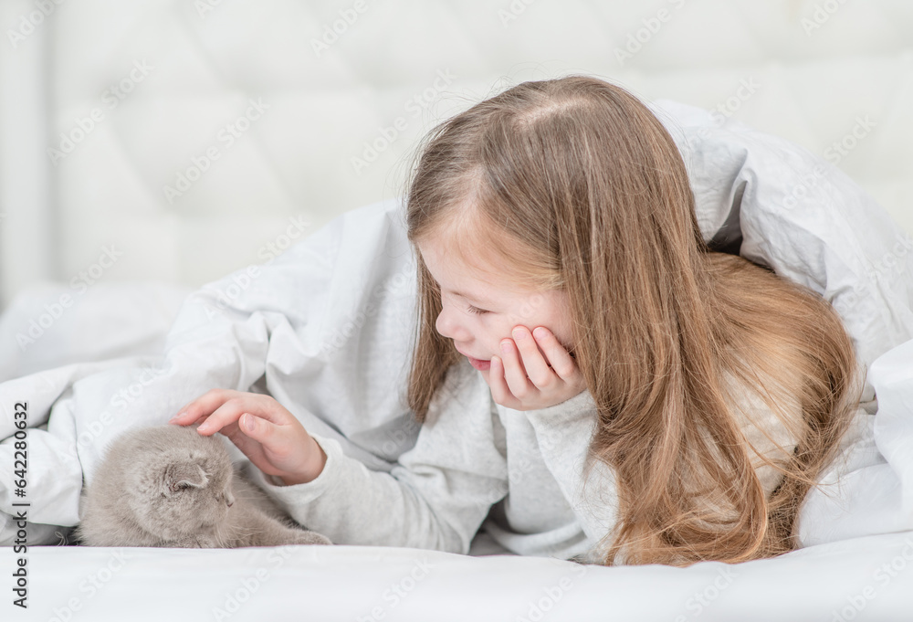 Happy little girl petting tiny kitten on the bed at home Happy little girl petting tiny kitten on the bed at home