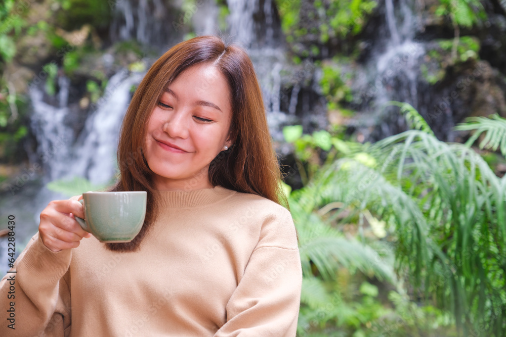 Portrait image of a young woman holding and drinking coffee while sitting in the garden with waterfall Portrait image of a young woman holding and drinking coffee while sitting in the garden with waterfall