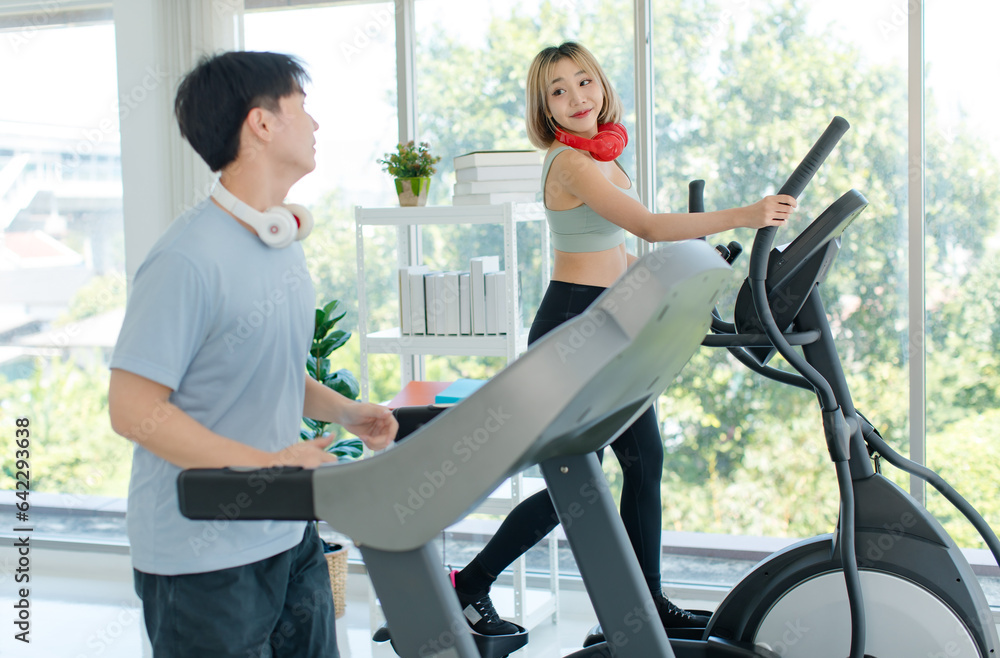 Asian young fit male female athlete jogger runner in sportswear sport bra legging wear wireless headphones smiling holding hands high five while exercise training on treadmill and elliptical machine Asian young fit male female athlete jogger runner in sportswear sport bra legging wear wireless headphones smiling holding hands high five while exercise training on treadmill and elliptical machine