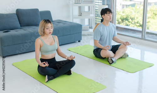 Asian young fit male female husband and wife in sportswear sport bra legging sneakers sitting closed eyes meditating on yoga mat with lotus posture exercising training together in living room at home