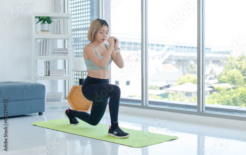 Asian young pretty fit female athlete teenager in sportswear sport bra leggings standing on yoga mat doing lunge stretching legs warming up working out practicing training exercising in living room.