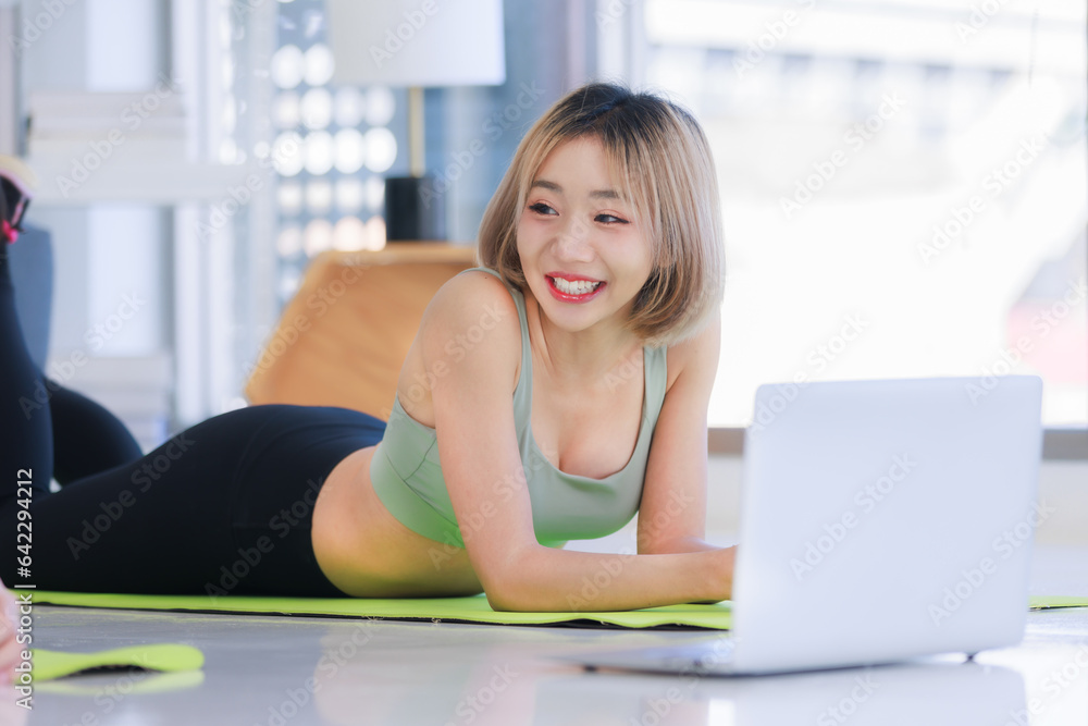 Asian young beautiful female athlete teenager in sportswear sport bra legging lay down relax exercising practicing browsing laptop notebook computer on yoga pilates in living room Asian young beautiful female athlete teenager in sportswear sport bra legging lay down relax exercising practicing browsing laptop notebook computer on yoga pilates in living room