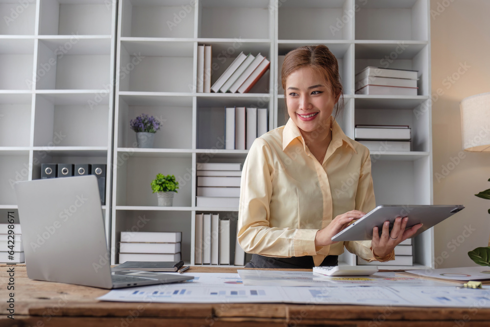 Beautiful and happy young Asian businesswoman looking at her laptop screen while enjoying her morning coffee at her desk in the office. Beautiful and happy young Asian businesswoman looking at her laptop screen while enjoying her morning coffee at her desk in the office.
