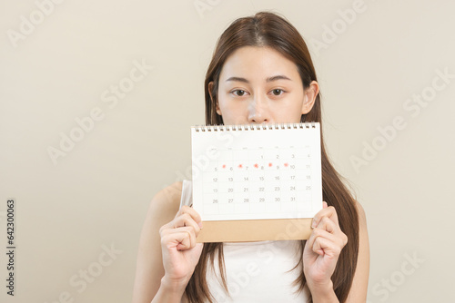 Menstruation, periods cycle day of monthly, hurt asian young woman, female hand holding, marking symbol on calendar for missed and delay or late. Medical, healthcare, gynecological concept. Copy space photo