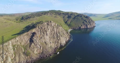 The rocky cliff on the Baikal coastline. It's a sunny day, the sky is clear. The drone flies near the rocky cliff photo