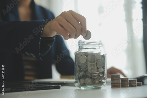 saving money and accounting concept. business man putting coin insert to jar and make acounting book for finance management to investment and saving. photo