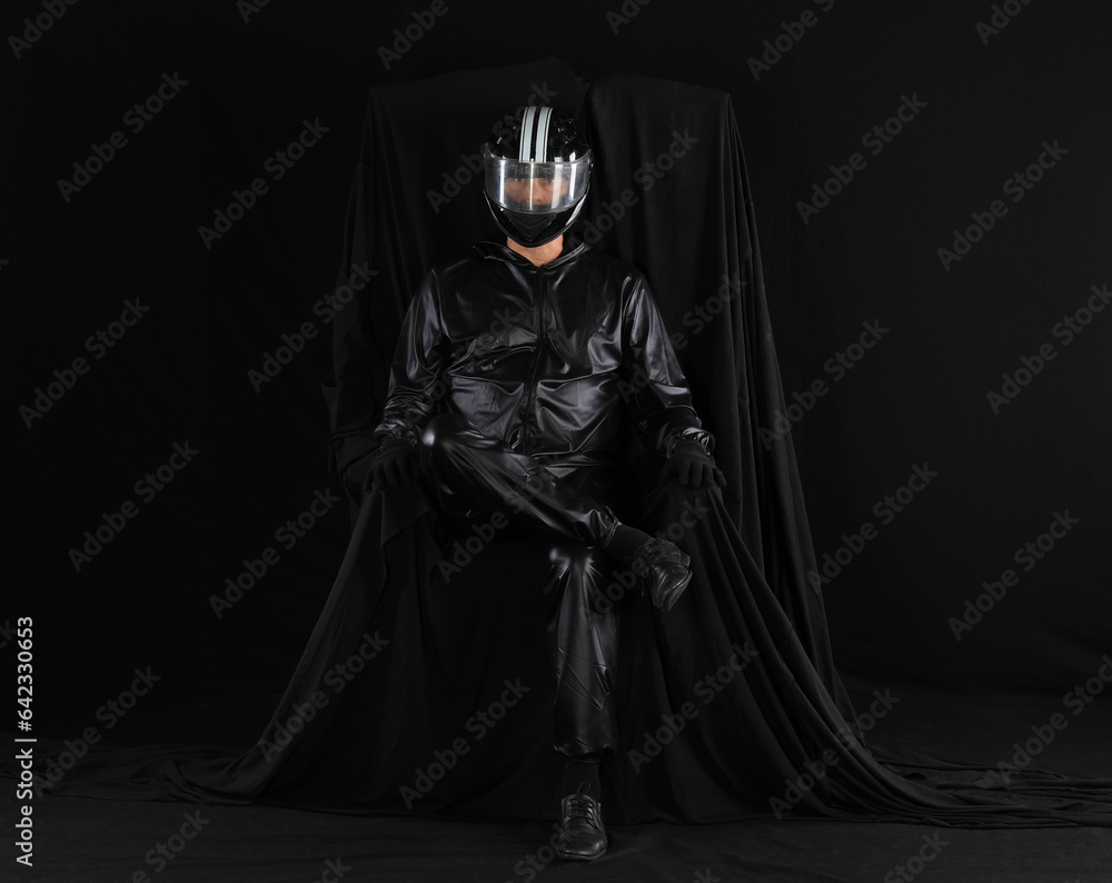 portrait of a biker in a helmet on a chair on a black background portrait of a biker in a helmet on a chair on a black background