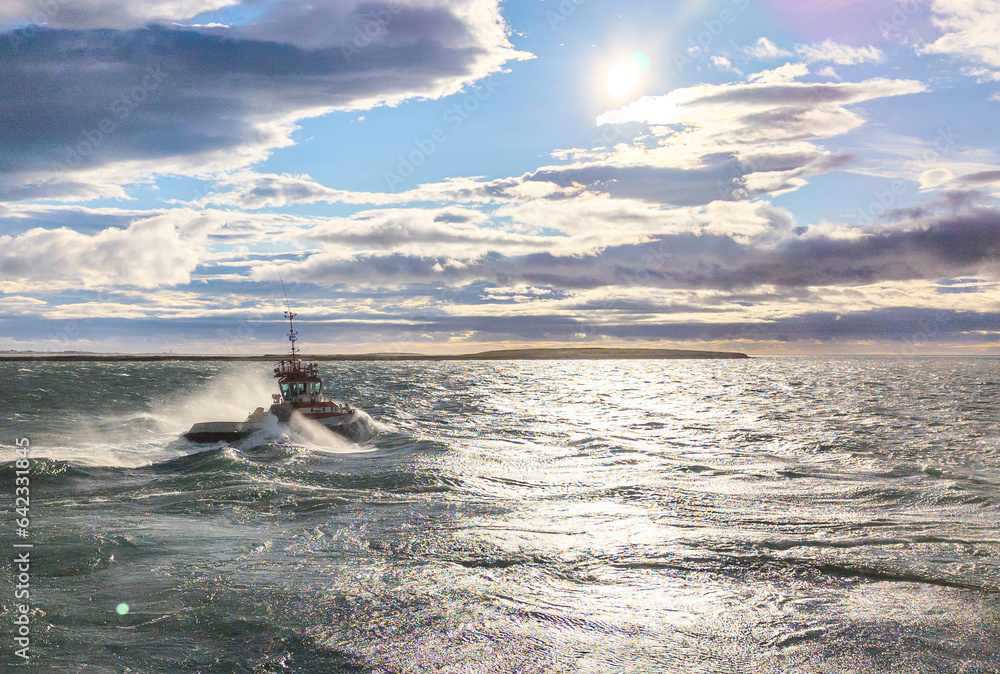 Tug boat on the ocean at rough sea with the sun and an island in the background - Landscape Photography