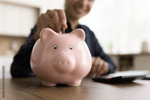 Smiling young business professional manager woman enjoying financial management, investment, saving money, throwing cash into ceramic piggy bank for getting profit, future income