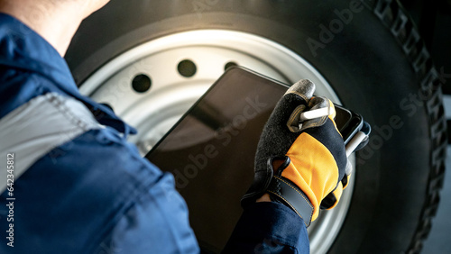 Tyre service and car suspension system maintenance for safe driving. Male hand auto mechanic in yellow protective gloves using digital tablet checking car wheel and rubber tire in auto repair shop