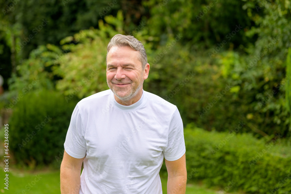 Man in his 50s with a mischievous smile while standing in the garden Man in his 50s with a mischievous smile while standing in the garden