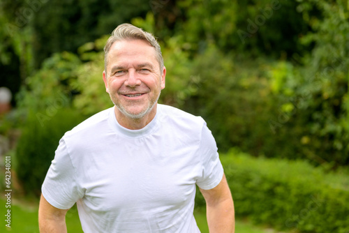Man in his 50s with a mischievous smile while standing in the garden